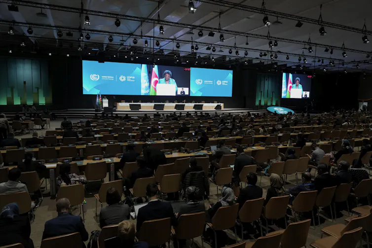 People sit at tables while a woman at a podium gives a speech.