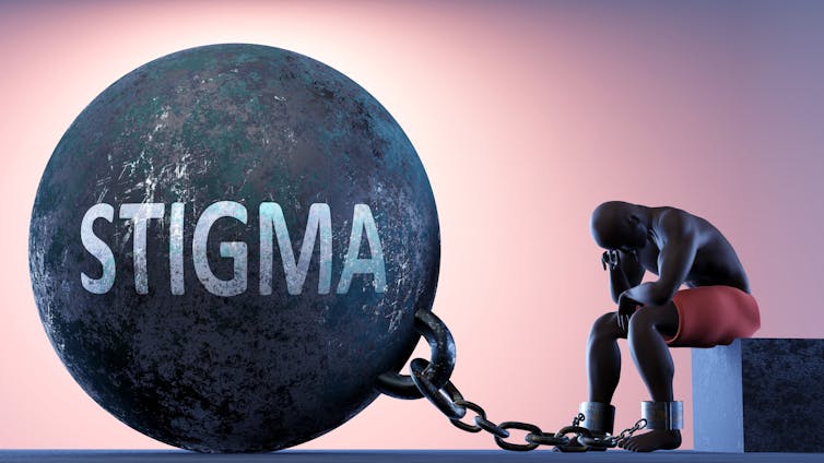 A man sitting on a block with his head in hand, with a very large ball and chain labelled 'stigma' attached to his ankle