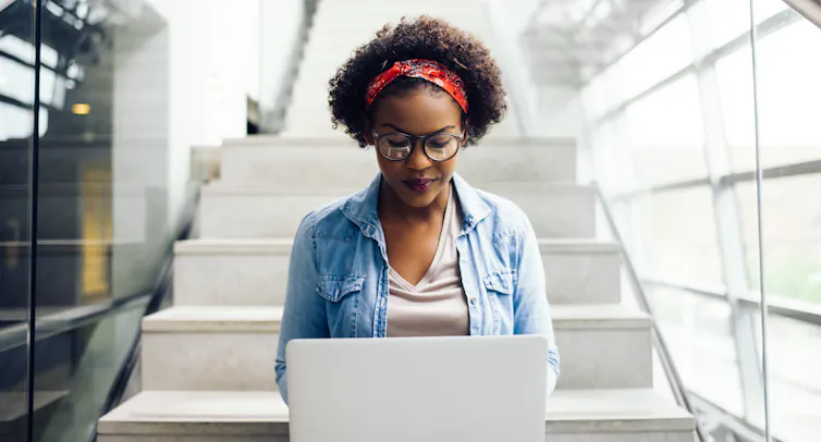A young woman works on a laptop while sitting on a set of stairs