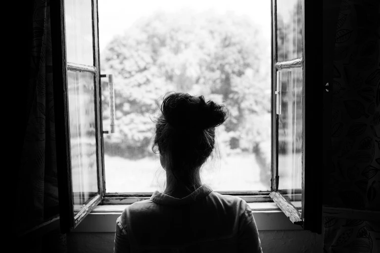 A young woman looks out of a window. Her back is to the camera.
