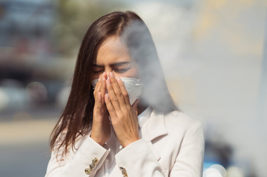 A woman wearing a mask covers her mouth and nose as air pollution or smoke wafts into her face.