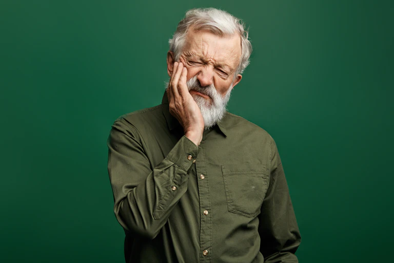 Man with a grey beard holding his face in agony.