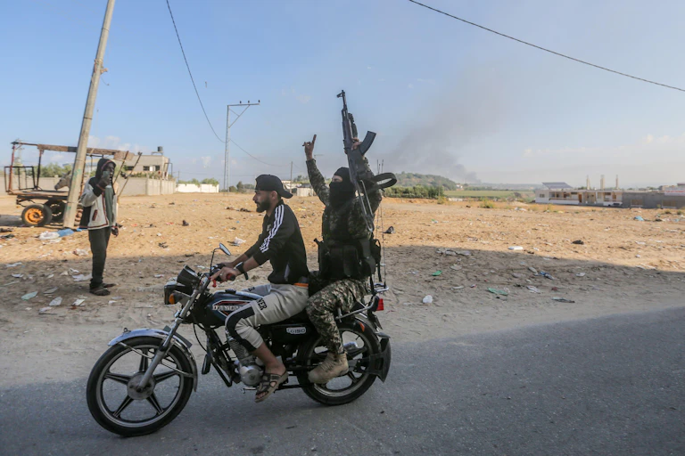 Hamas fighters ride a motorcycle. The passenger is carrying an automatic rifle.