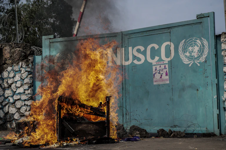 Départ de feu devant un portail sur lequel se trouve le sigle de l'ONU et l'inscription "MONUSCO"