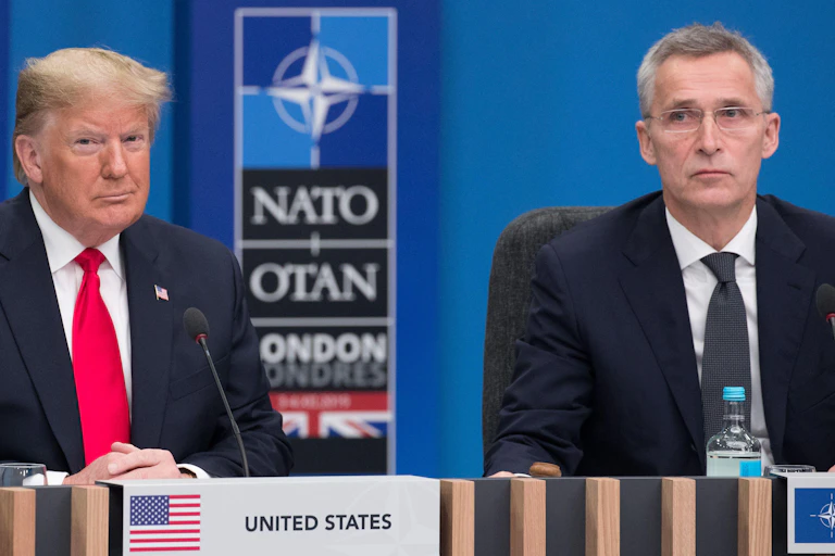 Donald Trump sitting at a desk with a Nato sign behind him.