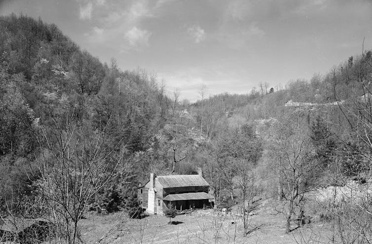 Black and white photo of small house surrounded by hilly terrain.