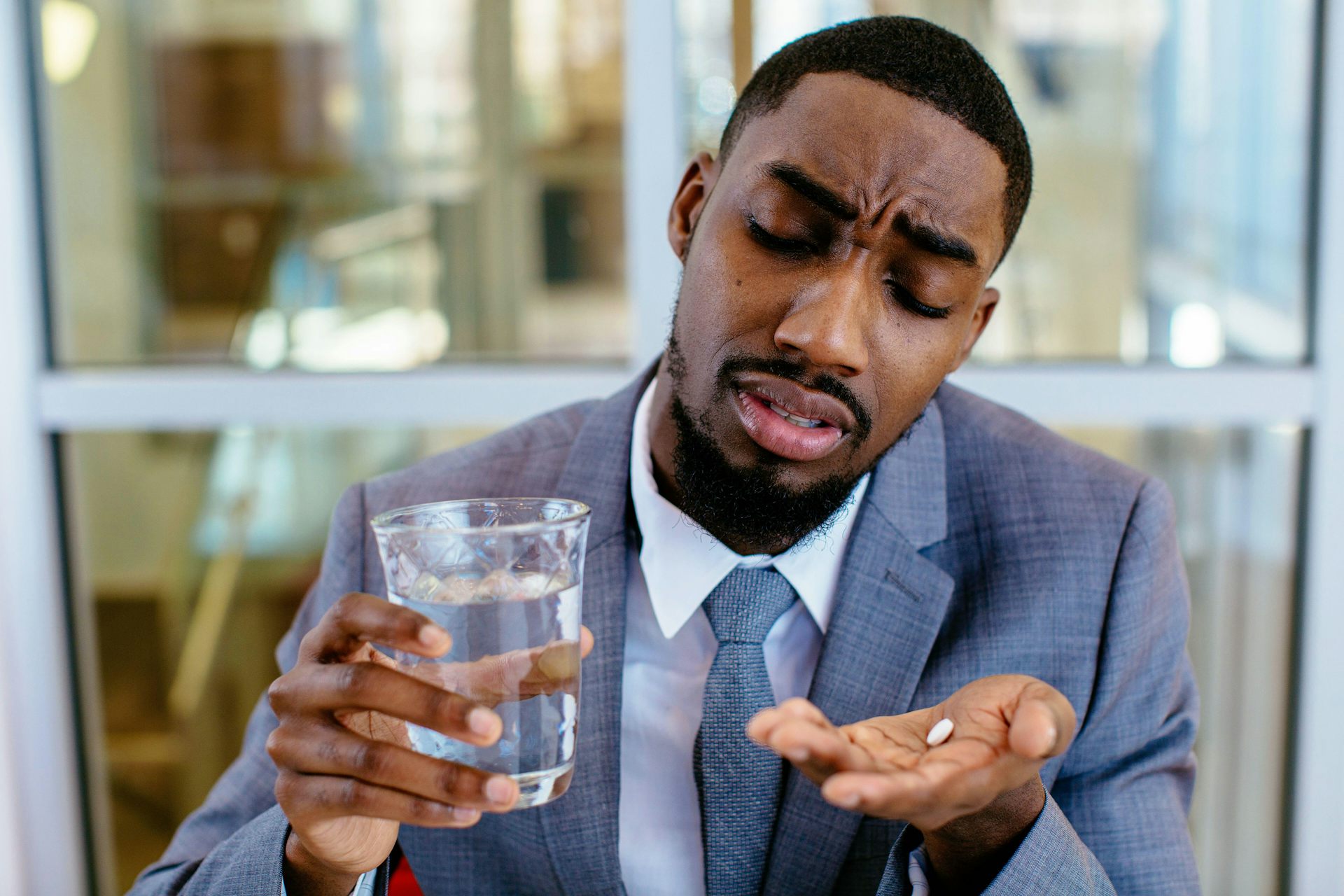 A sick looking man in a suit about to swallow a pill.