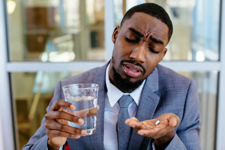 A sick looking man in a suit about to swallow a pill.