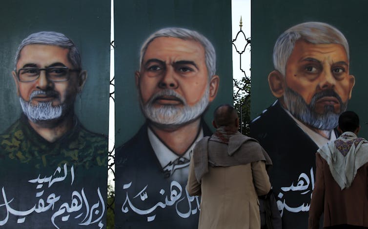 People look at paintings depicting Yahya Sinwar, Ismail Haniyeh and Ibrahim Aqil.