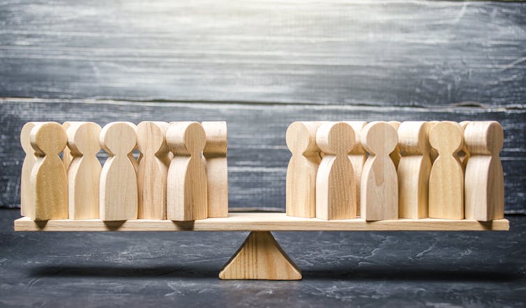 A wooden teeter-totter on which are balanced groups of wooden figures, making things even.