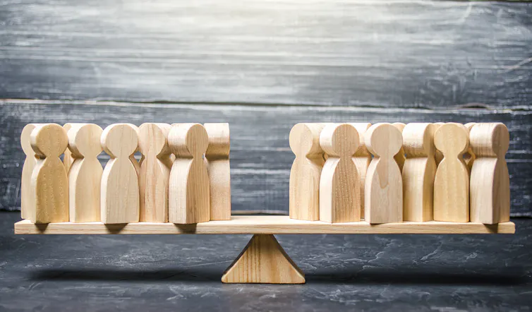 A wooden teeter-totter on which are balanced groups of wooden figures, making things even.