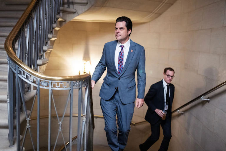 A man in a light gray suit climbing a staircase with a brass railing.