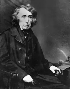 A vintage photo of a dark-haired man in dark clothes, sitting in a chair.