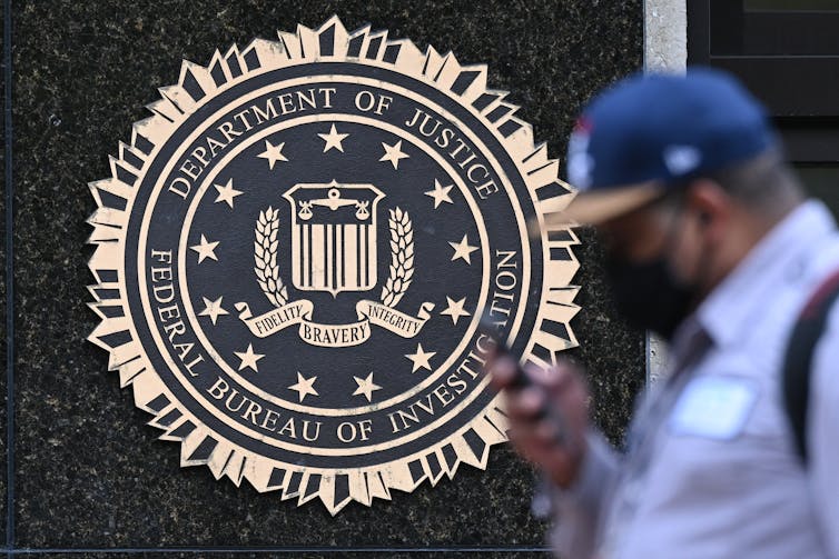 A pedestrian walks past a seal on a building reading 'Department of Justice Federal Bureau of Investigation.'