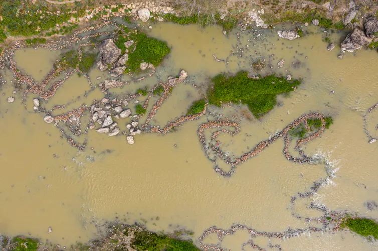 Aerial view of river with patterned lines of rocks in the water.