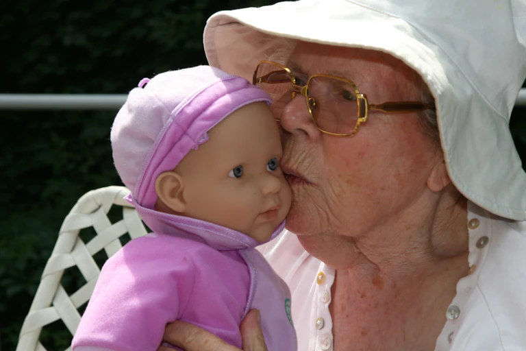Older woman in a white hat kisses a baby doll