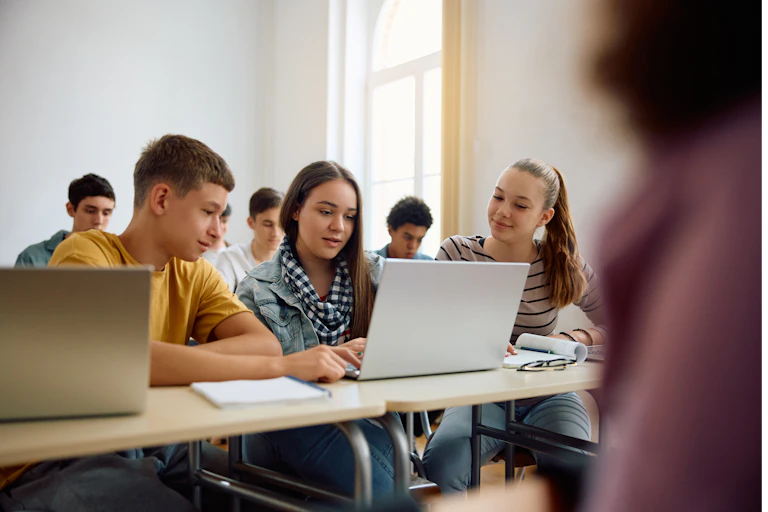 Teenagers working on a laptop in a classroom.