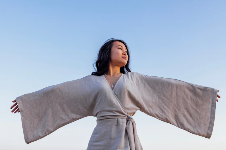 A woman wearing a linen kimono spreads her arms against the blue sky.