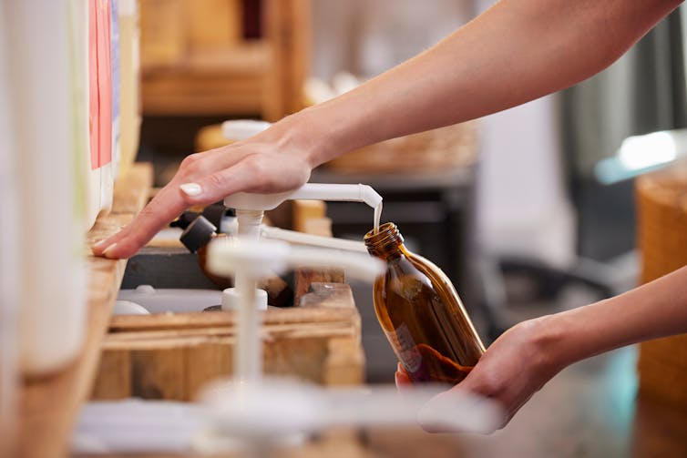 close up of woman's hands refilling bottle in zero waste shop