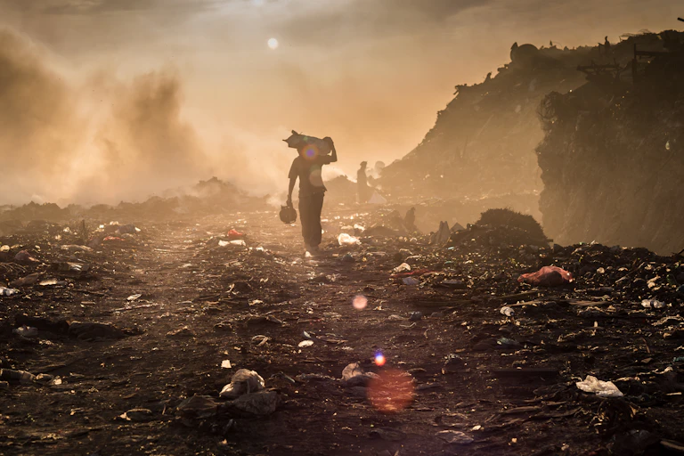 man holding waste on a dump, smoky brown sky
