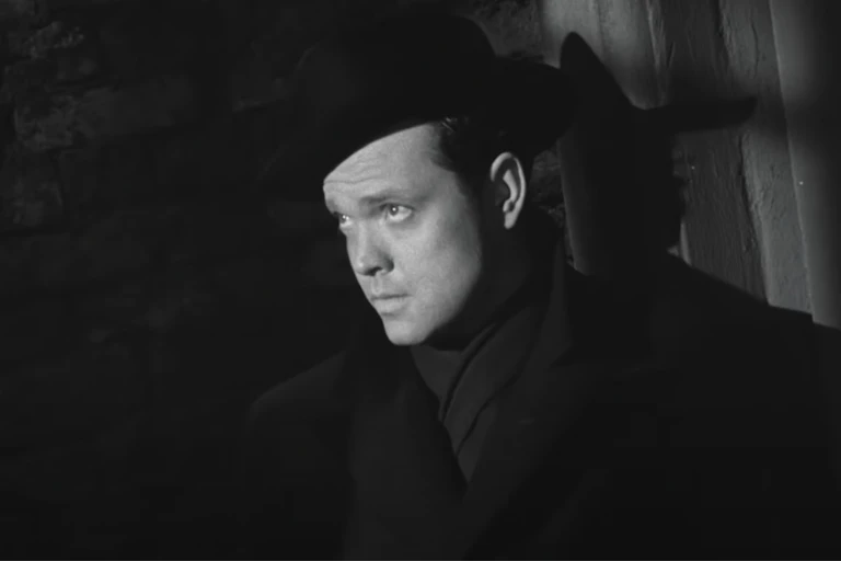 A man standing in the shadows, only his face illuminated.
