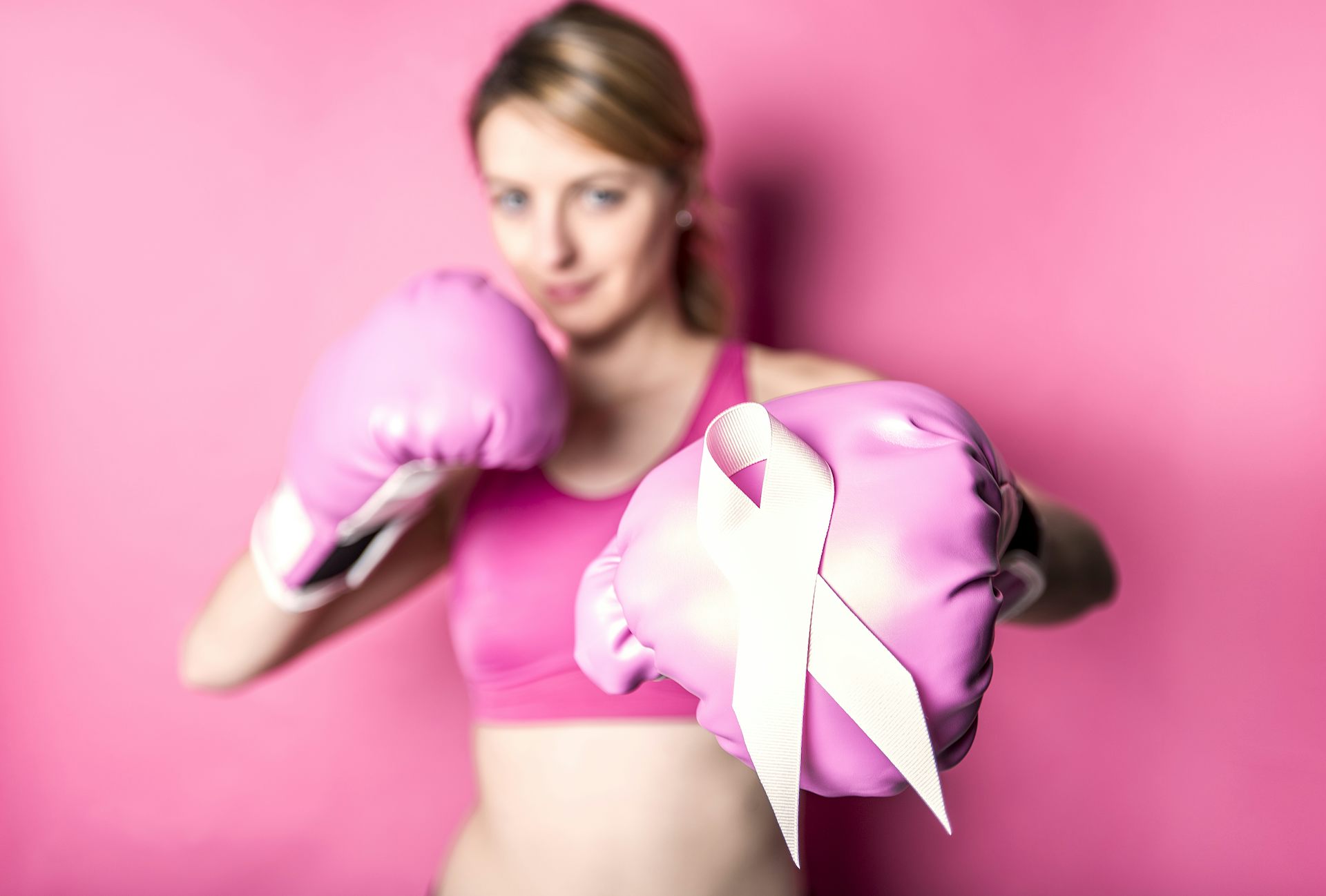 A woman in sportswear wears boxing gloves, with a pink October ribbon displayed on one of the gloves
