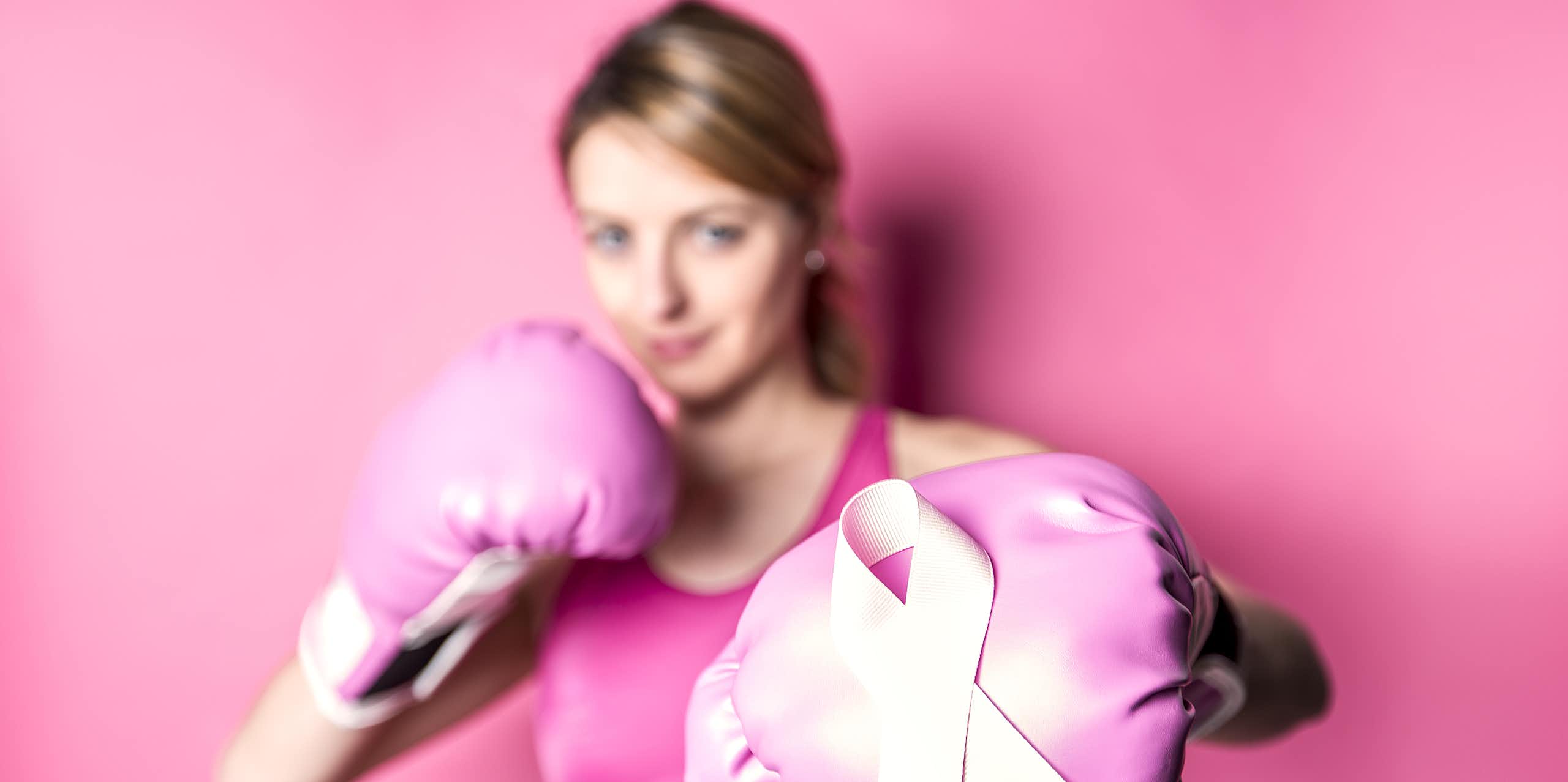 A woman in sportswear wears boxing gloves, with a pink October ribbon displayed on one of the gloves
