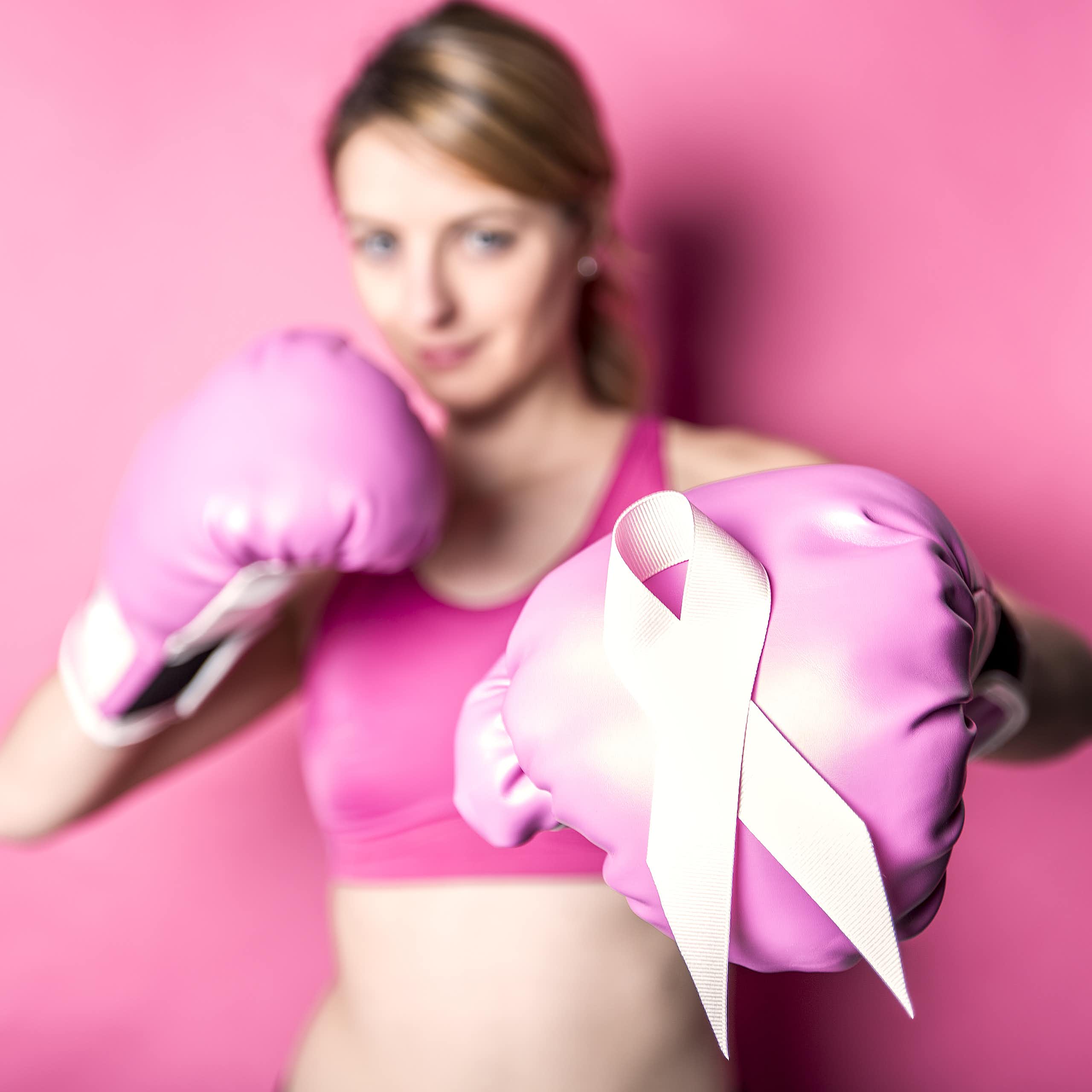 A woman in sportswear wears boxing gloves, with a pink October ribbon displayed on one of the gloves