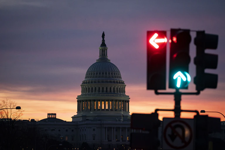 A dark sky with a large white building that has a spire on it, behind a traffic light.