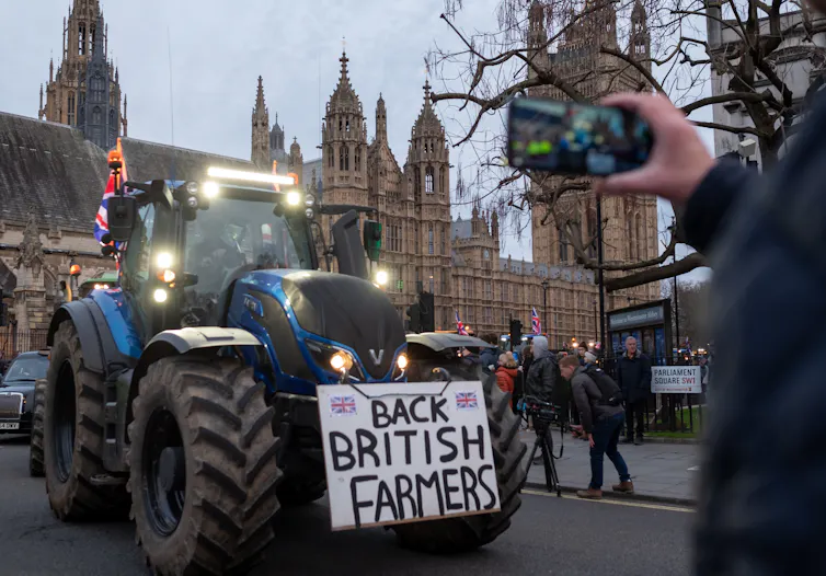 a tractor bearing a sign saying 'back british farmers' drives past Westminister