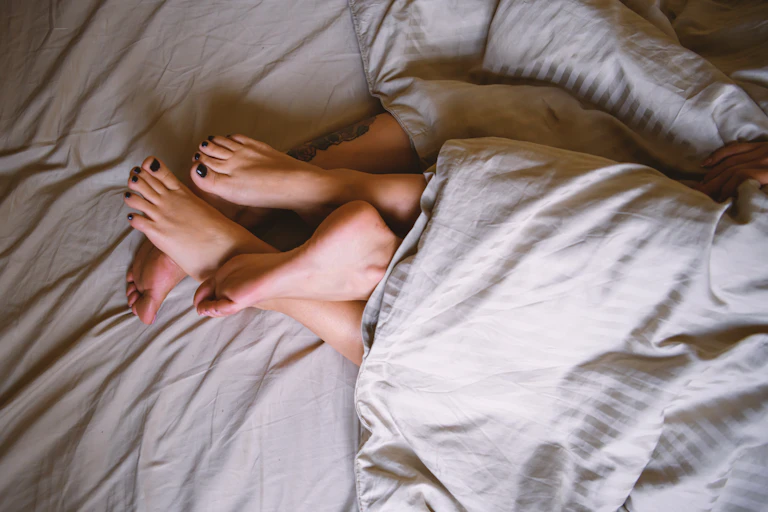 Intertangled feet of two women peek out from a duvet cover.