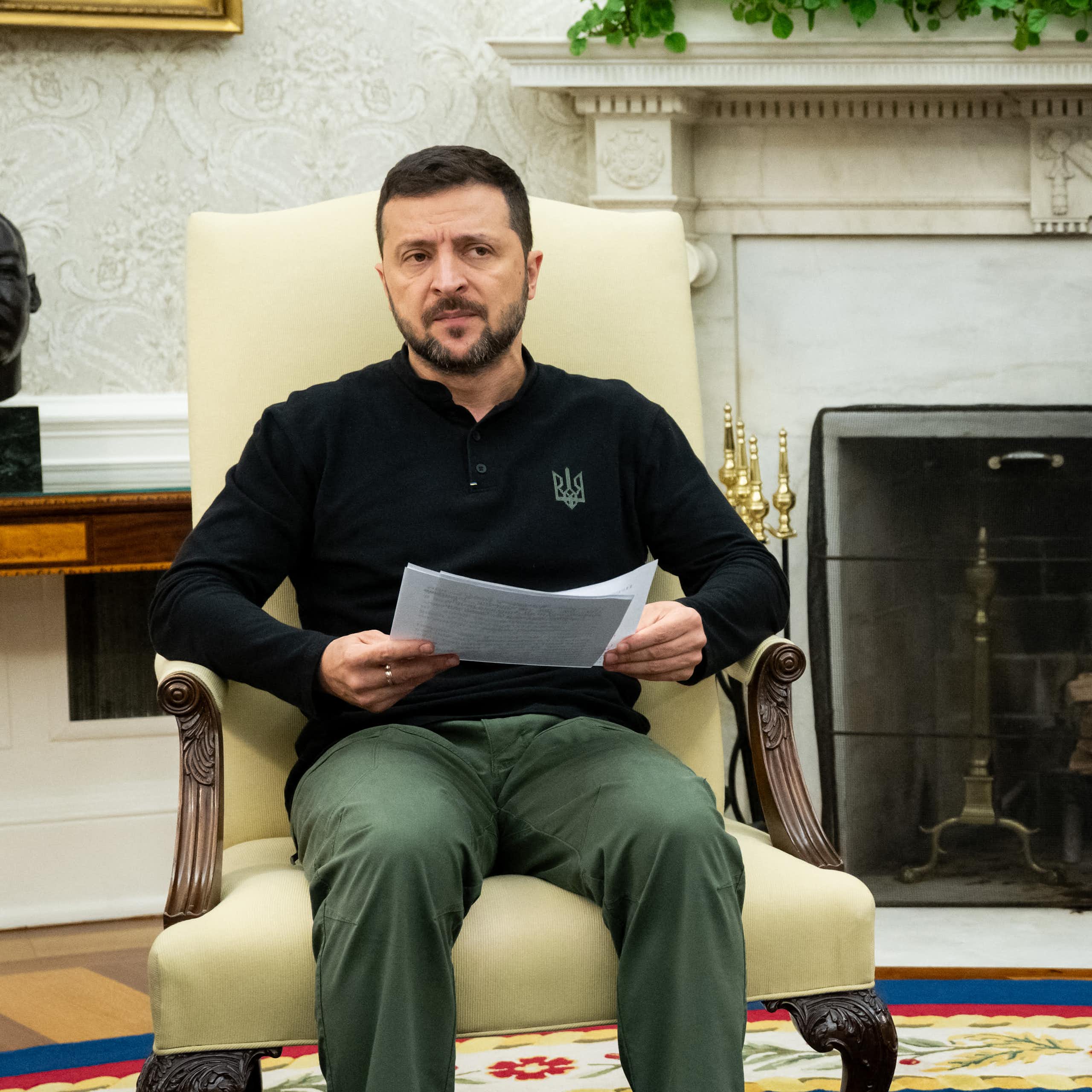 Two men, one in a suit, the other in a polo-neck shirt, sit on ornate chairs.