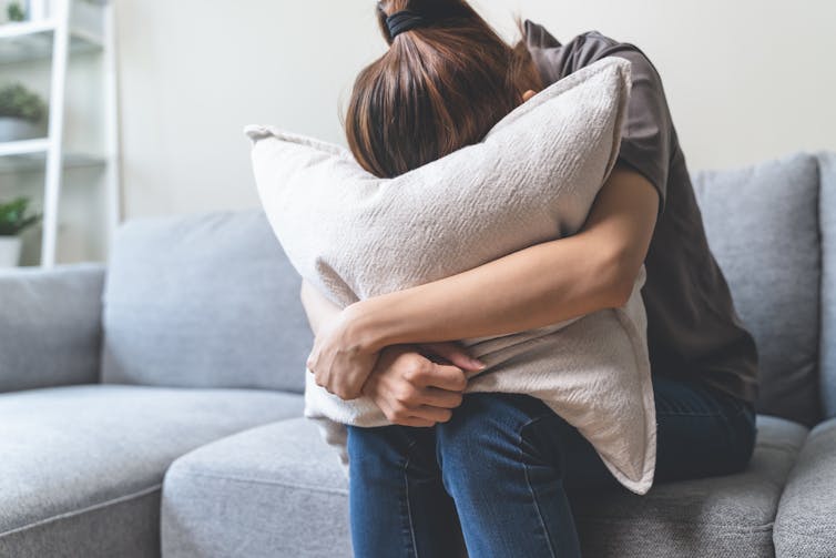 Woman covering her face with pillow in the living room at home.