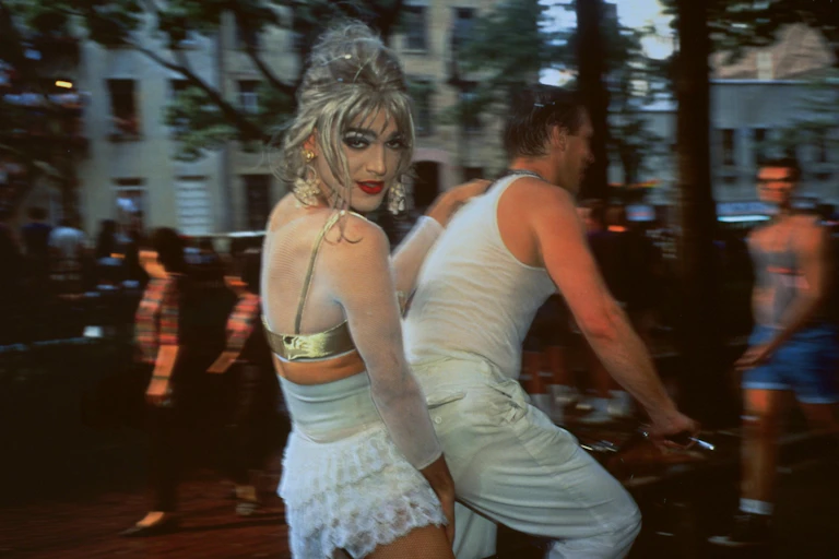 Two friends or lovers cycling together, one in a blonde wig looks to camera