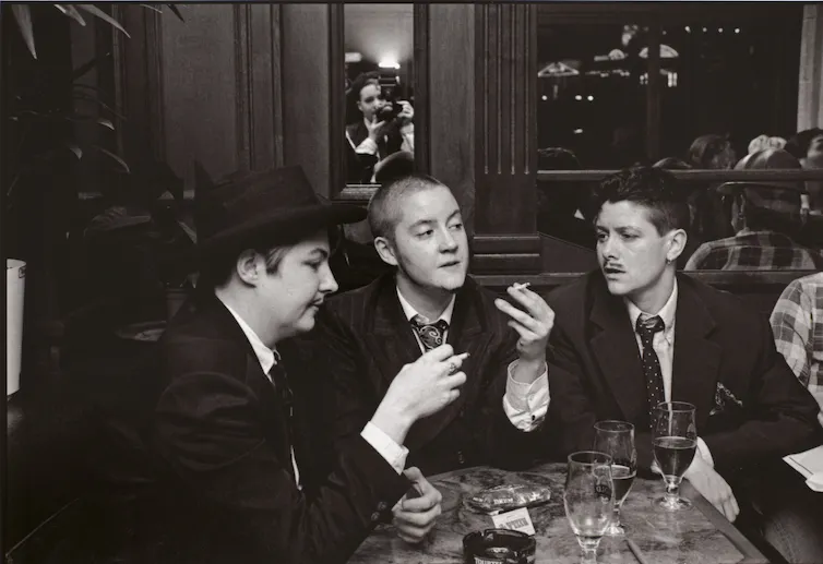 Three androgynous people wearing suits and smoking in a restaurant