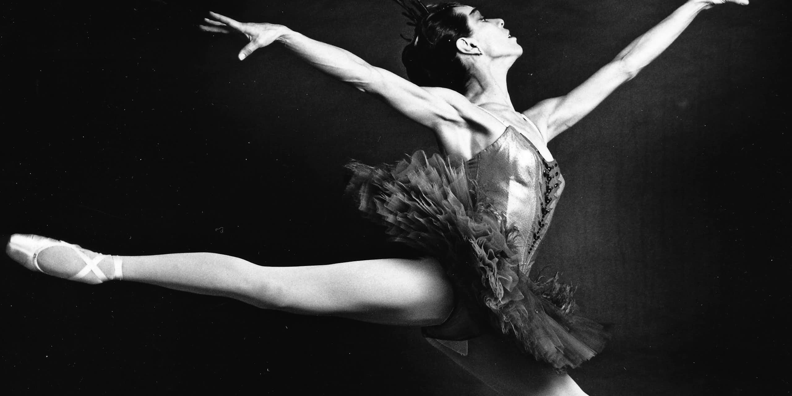 A ballet dancer taking a leap with her toes pointed outward and arms raised.