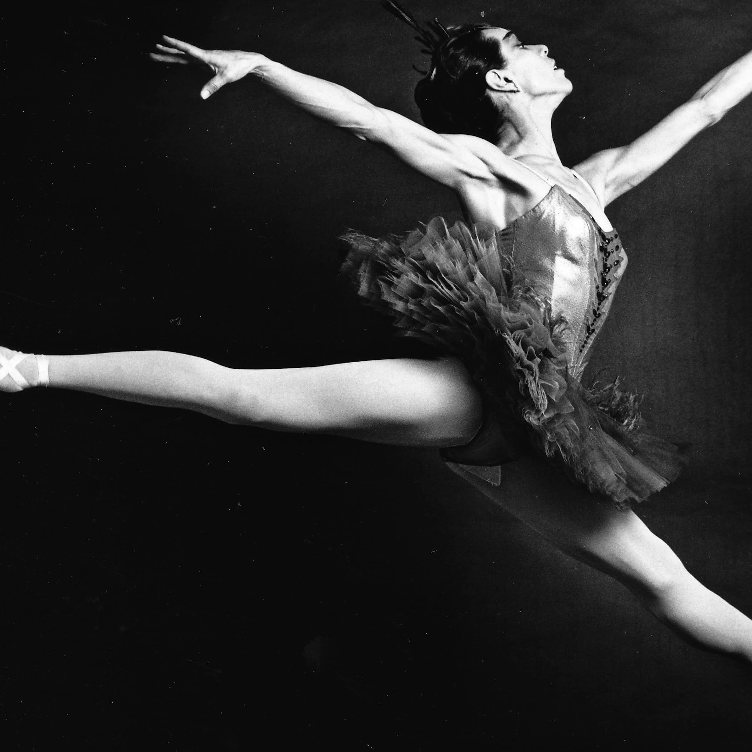 A ballet dancer taking a leap with her toes pointed outward and arms raised.