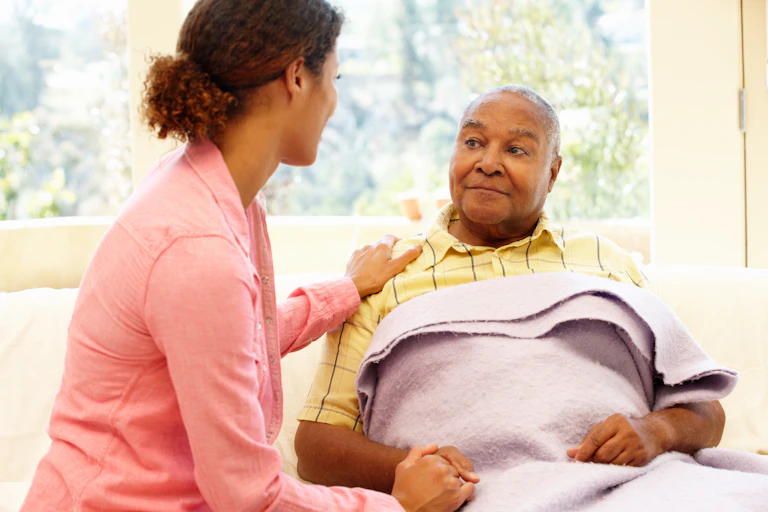 A older man with a blanket over him, and a younger woman with her hand on his shoulder