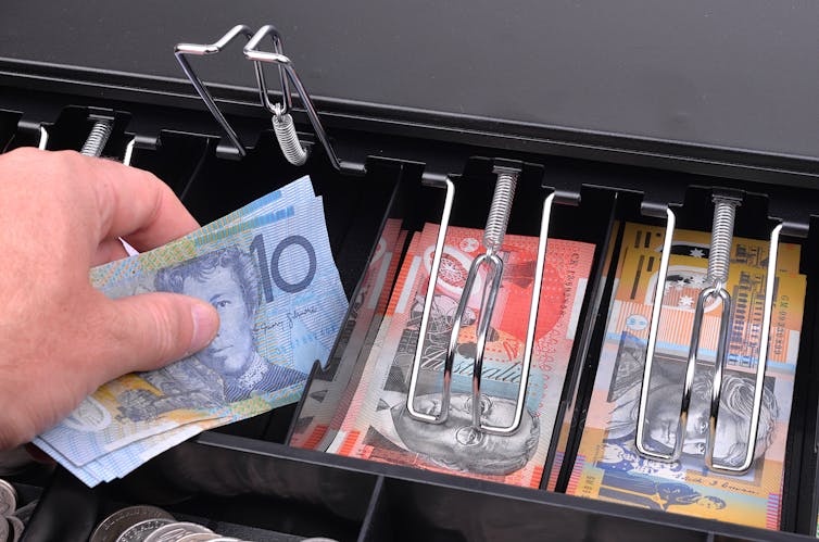 Hand taking an Australian ten dollar note from a cash register.