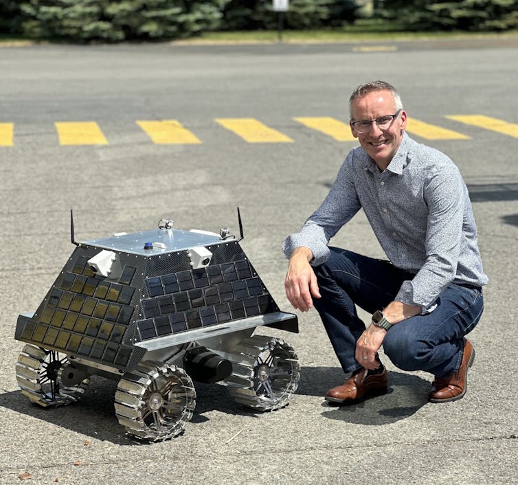 A man crouches next to a small space vehicle.