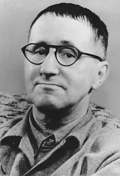 A man with short, cropped dark hair and round glasses.