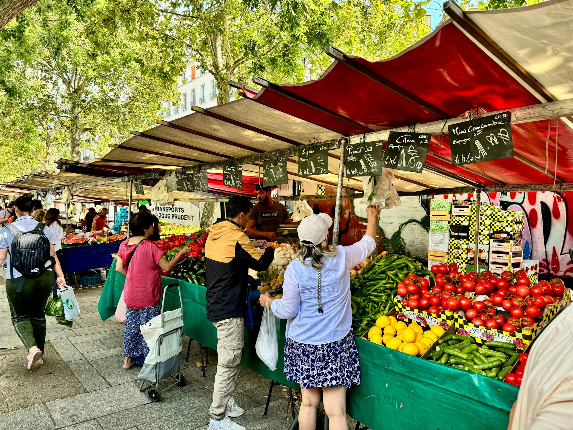 Image d'un marché en plein air avec un étal de fruits et légumes avec des ardoises sur lesquelles sont écrites des prix