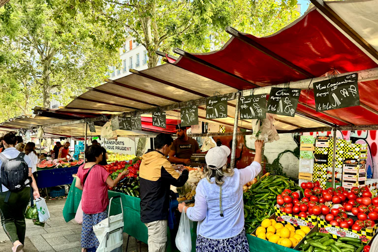 Image d'un marché en plein air avec un étal de fruits et légumes avec des ardoises sur lesquelles sont écrites des prix