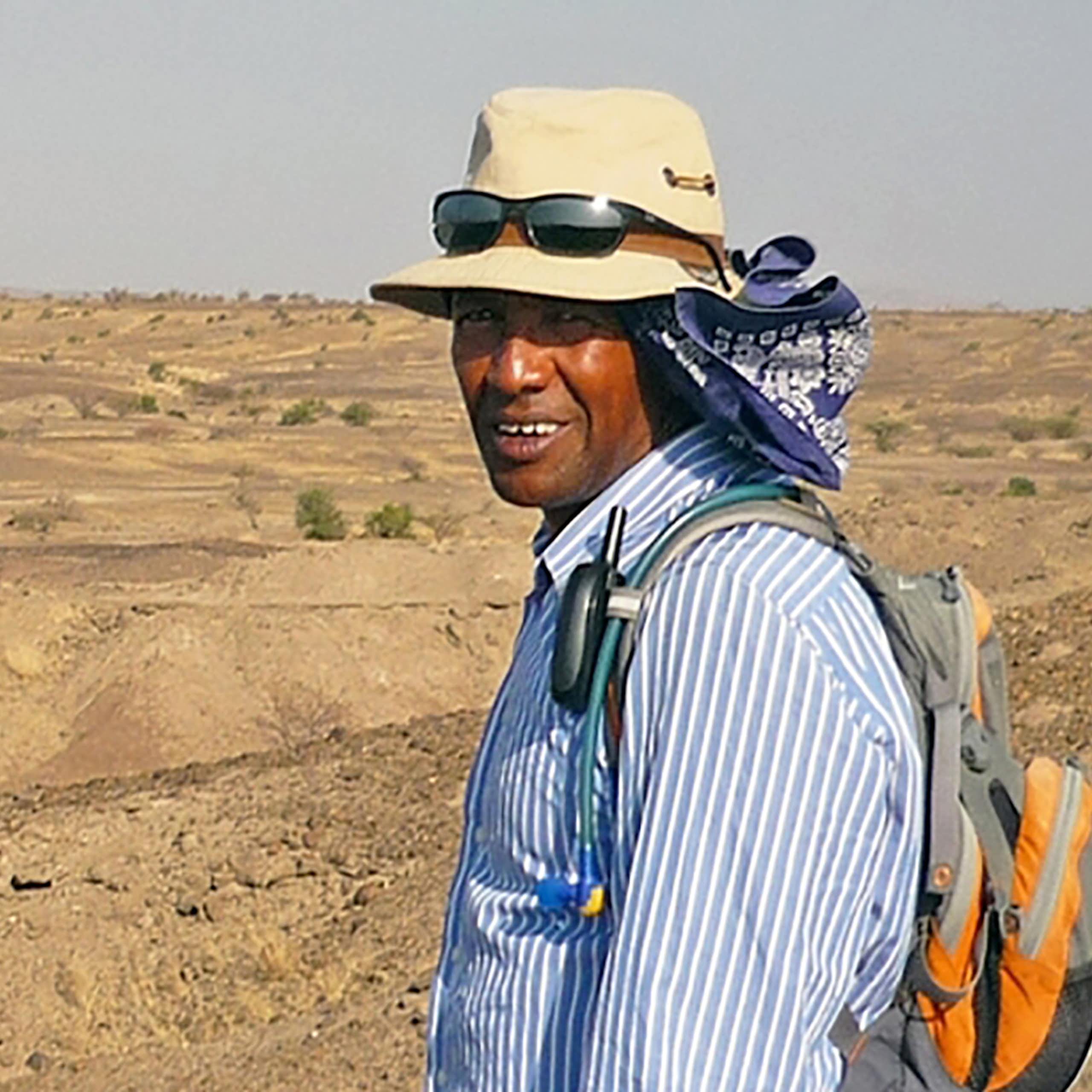 Scientist wearing a hat with desert landscape behind him