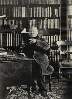Foto en blanco y negro de un hombre leyendo ante una estantería llena de libros.