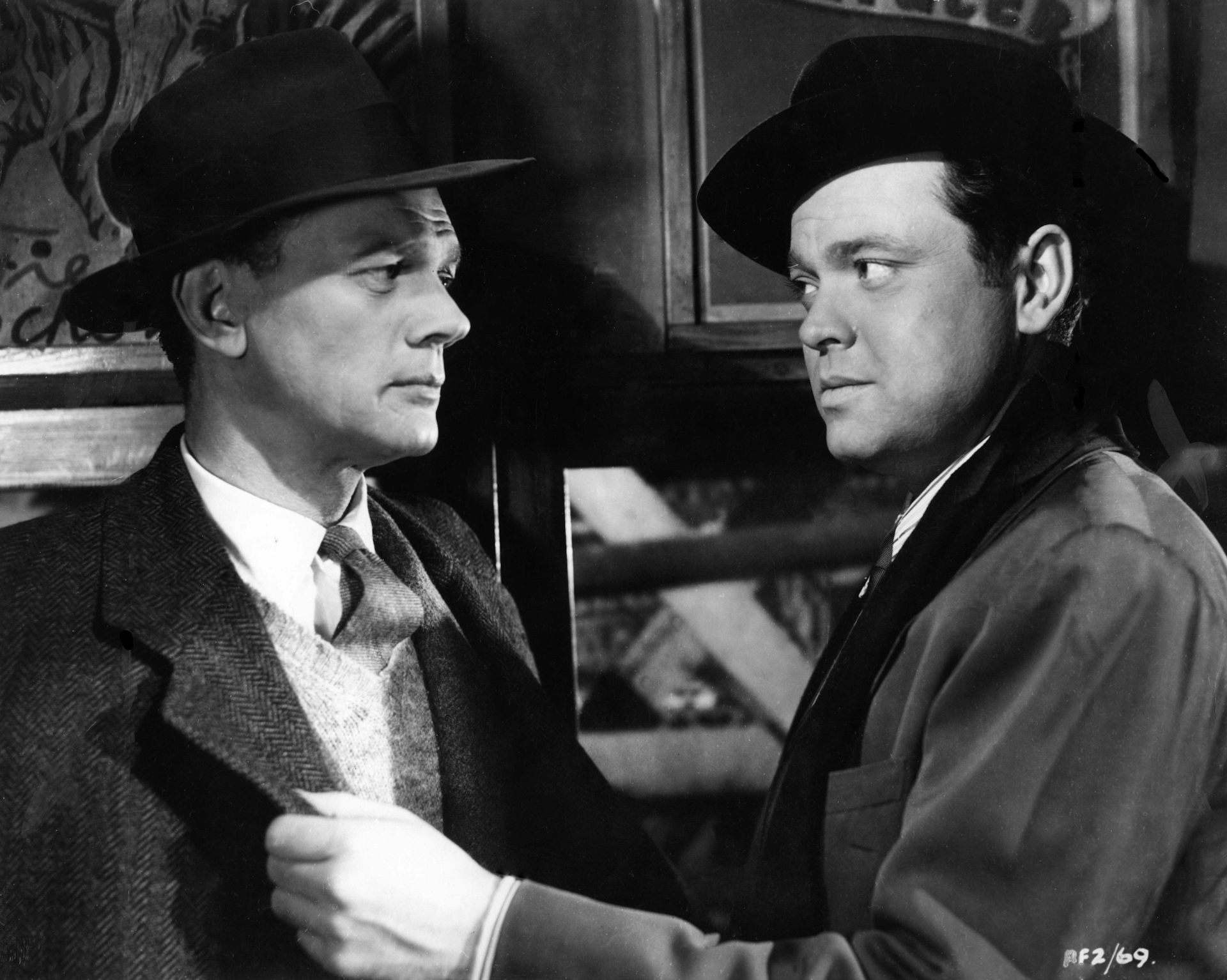 Black and white image of two men dressed in 1940s hats and overcoats.