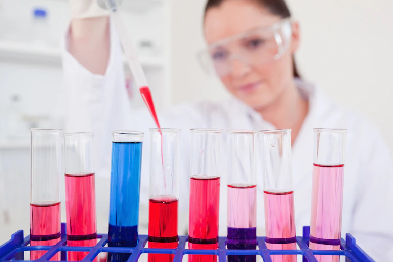 Une scientifique met du liquide à la pipette dans des tubes à essais remplis de liquides roses et bleus.