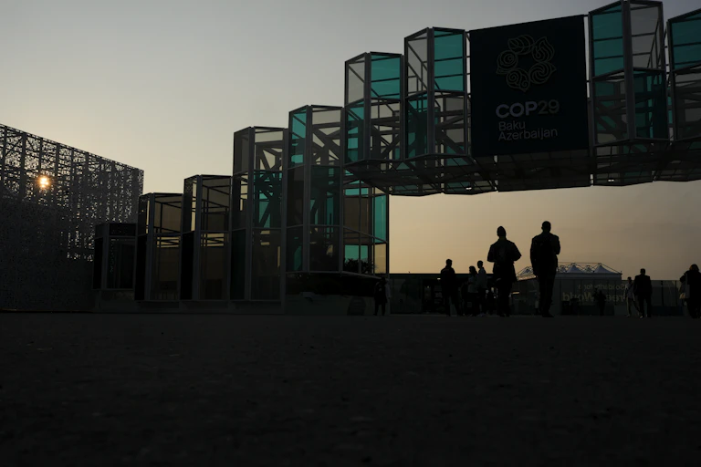 People walk under an arch-like structure at sunset.