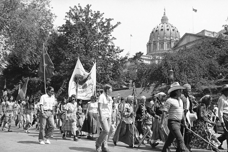 A black and white photo of marchers in warm weather passing a building with a high dome.