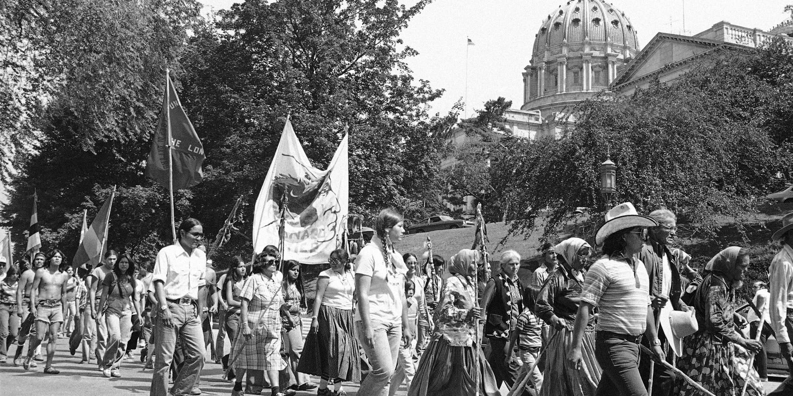 A black and white photo of marchers in warm weather passing a building with a high dome.